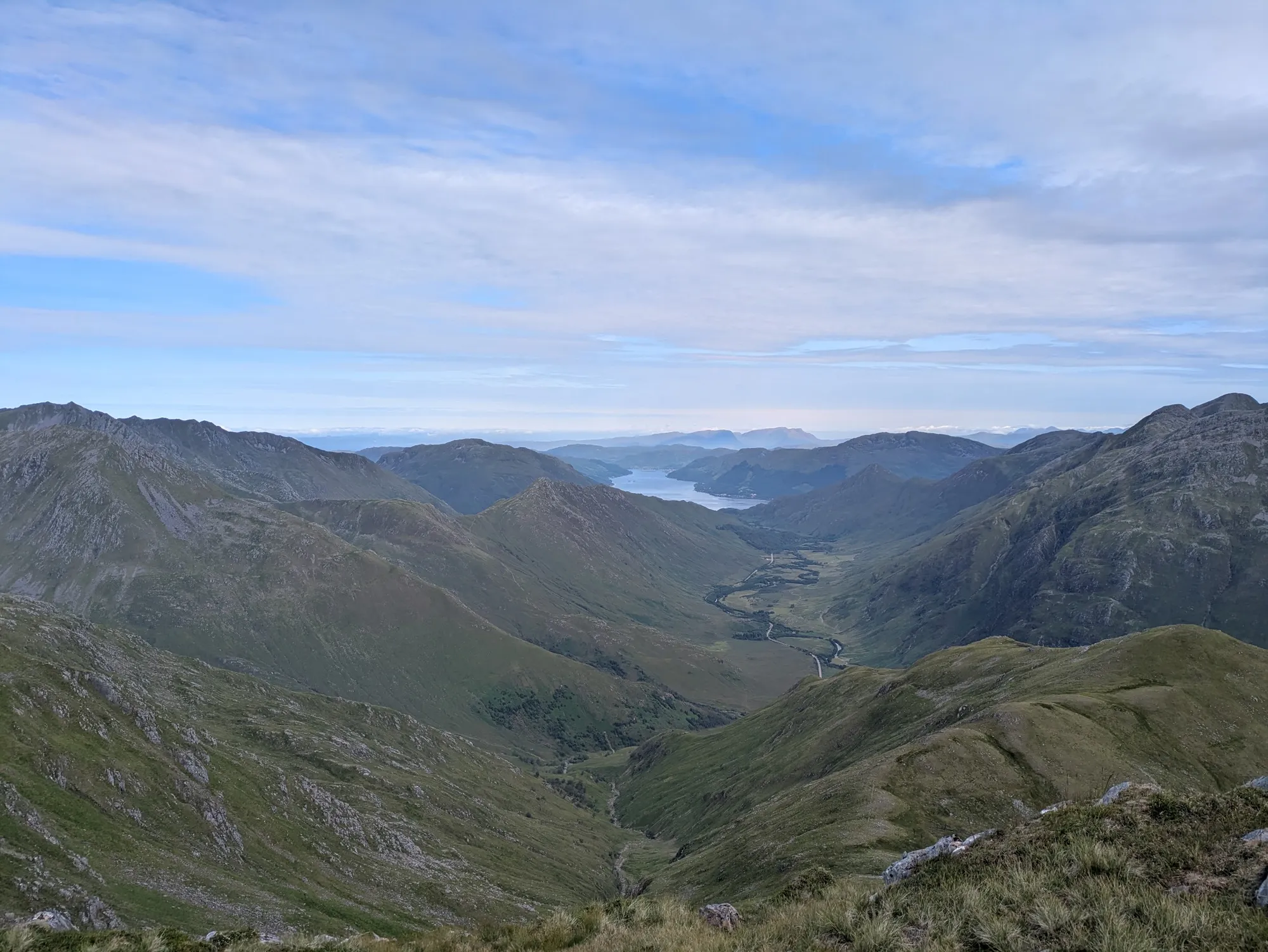 A Scottish glen falling away between grassy ridges to a sea loch, under high cloud