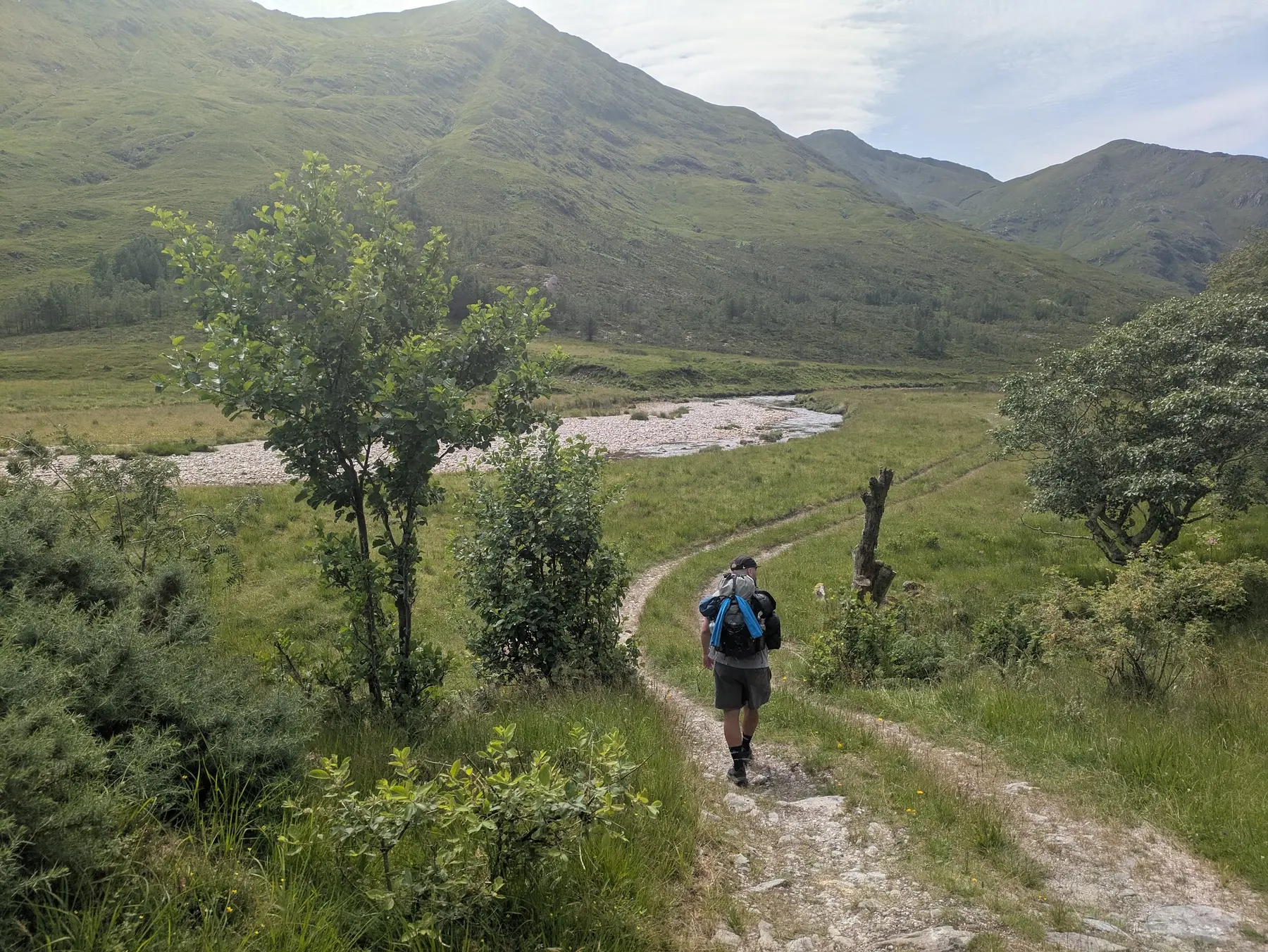 A backpacker walking beside a river through a mountain glen