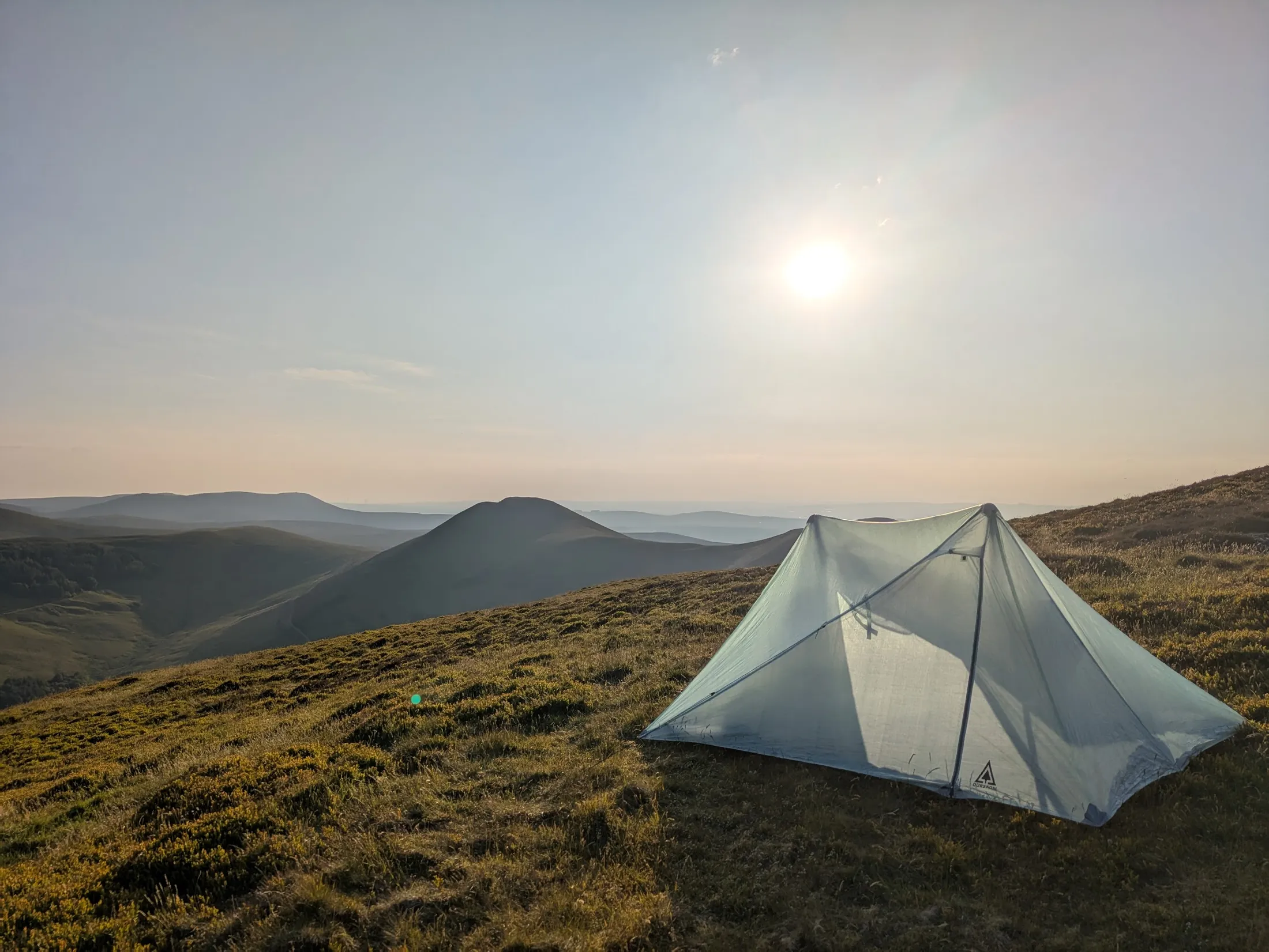 A backpacking tent glowing in the sun on a Scottish hillside